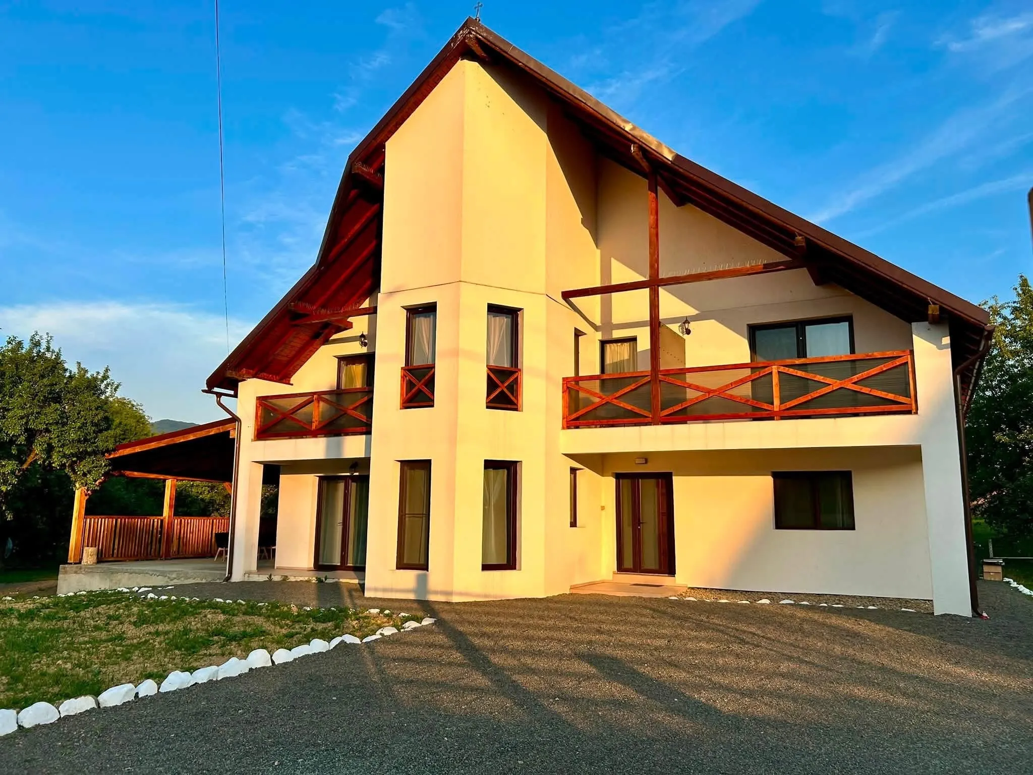 Vila Safir la apus, văzută din curte, cu fațada casei cu etaj, balcoane din lemn și terasa acoperită vizibilă în stânga